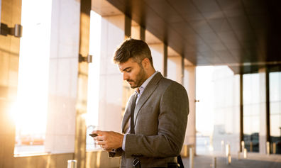 Man checks his phone outside a modern building at sunrise.