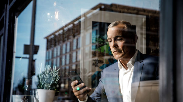 Man checks his phone outside a modern building at sunrise.
