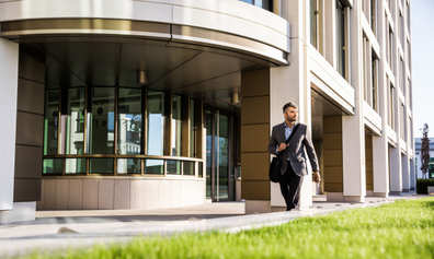 Man in a grey blazer walks out of a modern office building.