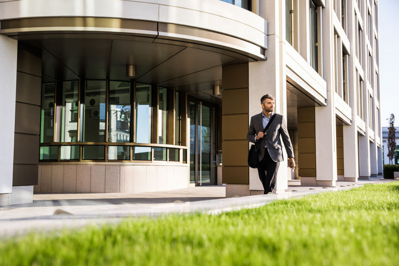 Man in a grey blazer walks out of a modern office building.