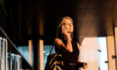 Woman takes a call outside a building during golden hour.
