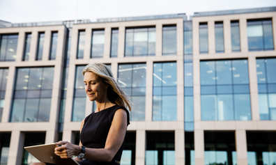 Woman works on a tablet outdoors in front of a corporate building.
