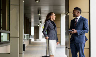 Two colleagues smiling and chatting in a modern outdoor office setting.