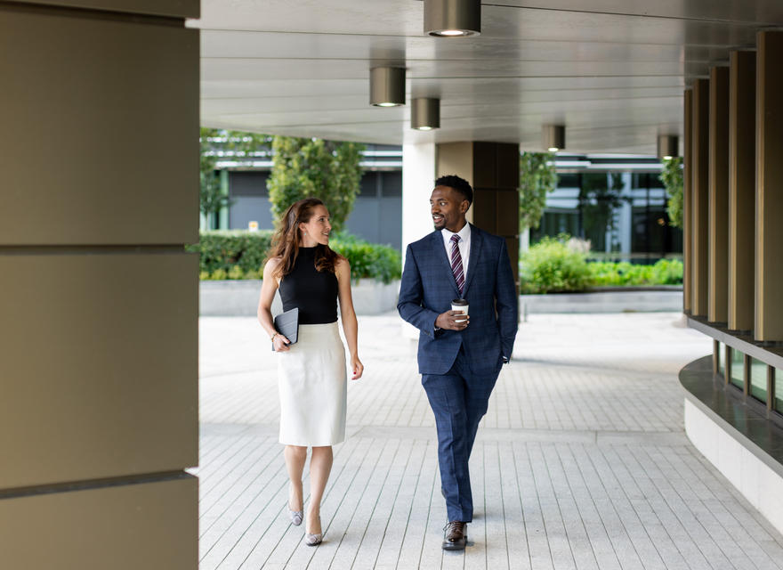 Two colleagues walking together outdoors, chatting and smiling.
