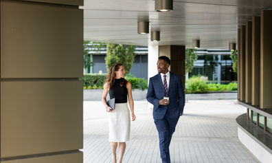 Two colleagues walking together outdoors, chatting and smiling.