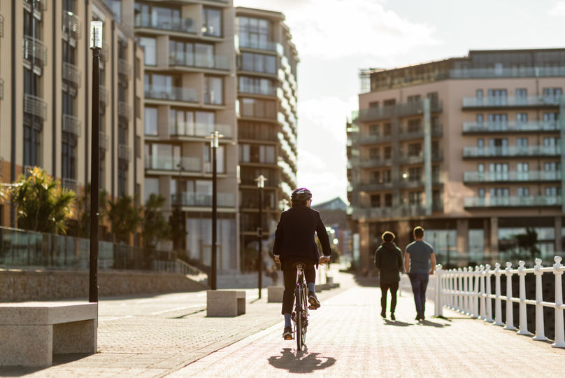 Businessman cycling away from camera along a modern waterfront promenade.