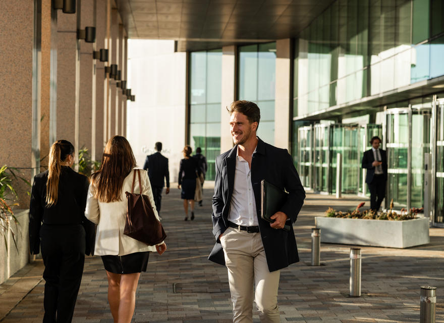 A smiling man walking through a corporate office space with colleagues in the background.