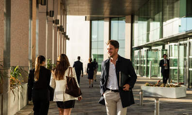 A smiling man walking through a corporate office space with colleagues in the background.