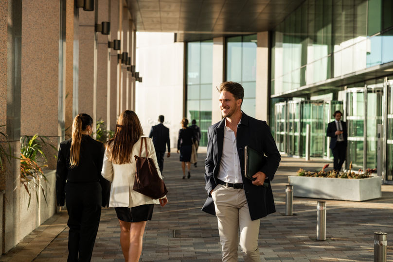 A smiling man walking through a corporate office space with colleagues in the background.