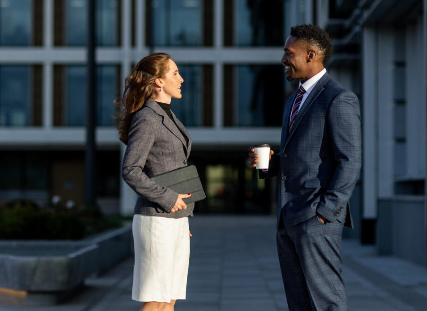 Two professionals talking while standing in a city plaza.