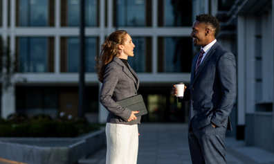 Two professionals talking while standing in a city plaza.