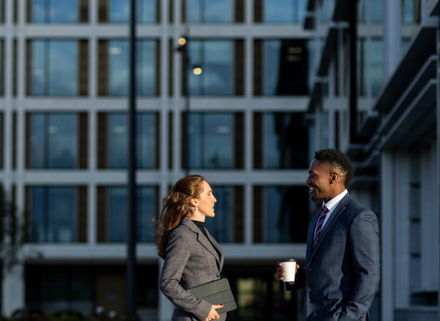 Two professionals talking while standing in a city plaza.