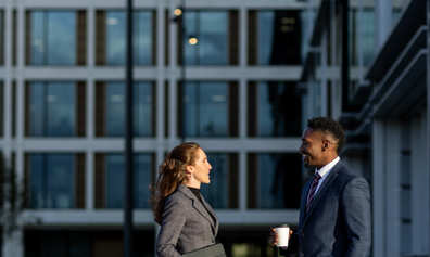 Two professionals talking while standing in a city plaza.