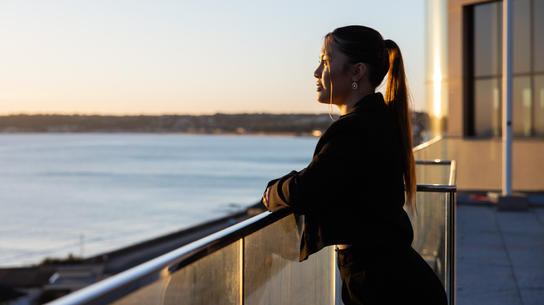 A female professional enjoys a peaceful moment overlooking the sunset from a rooftop terrace.