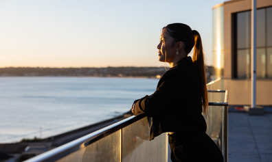A female professional enjoys a peaceful moment overlooking the sunset from a rooftop terrace.