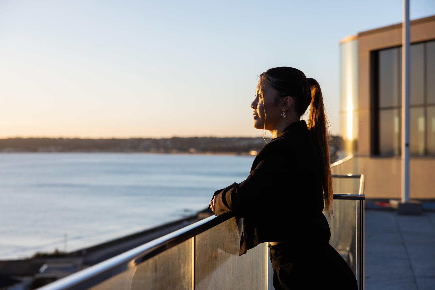 A female professional enjoys a peaceful moment overlooking the sunset from a rooftop terrace.