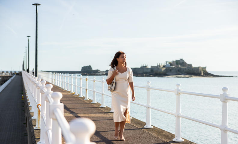 Woman walking along the seawall with Elizabeth Castle in the background.