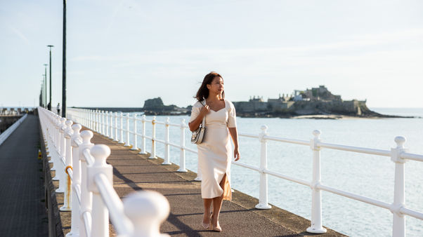 Woman walking along the seawall with Elizabeth Castle in the background.