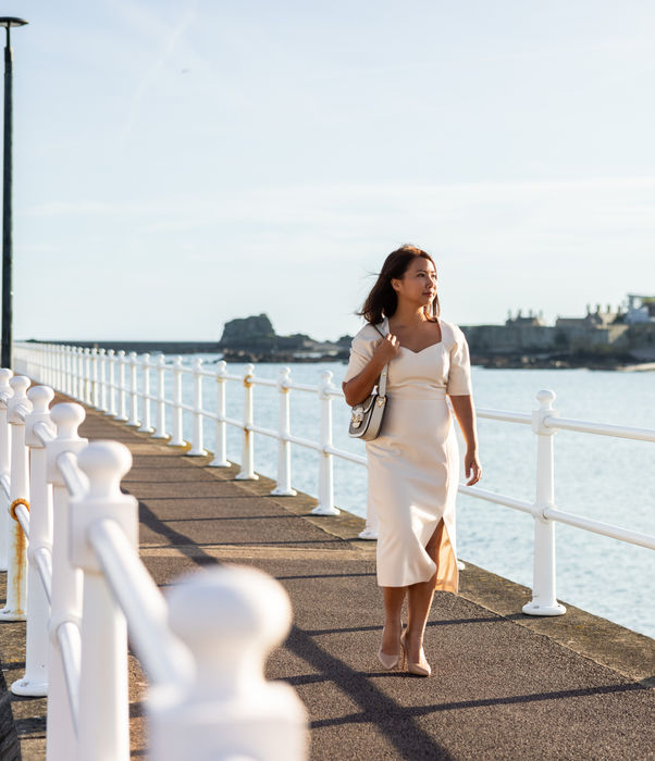 Woman walking along the seawall with Elizabeth Castle in the background.