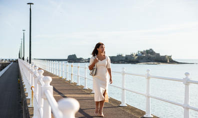 Woman walking along the seawall with Elizabeth Castle in the background.