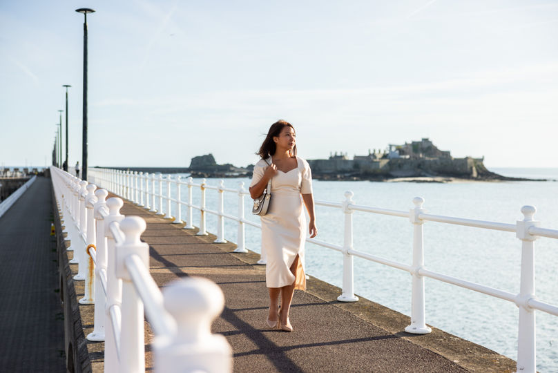 Woman walking along the seawall with Elizabeth Castle in the background.