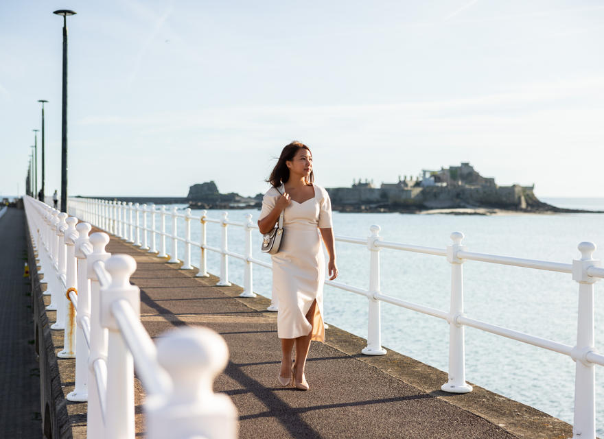 Woman walking along the seawall with Elizabeth Castle in the background.