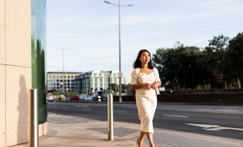 Businesswoman walking purposefully along a city pavement in soft evening light.
