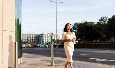 Businesswoman walking purposefully along a city pavement in soft evening light.