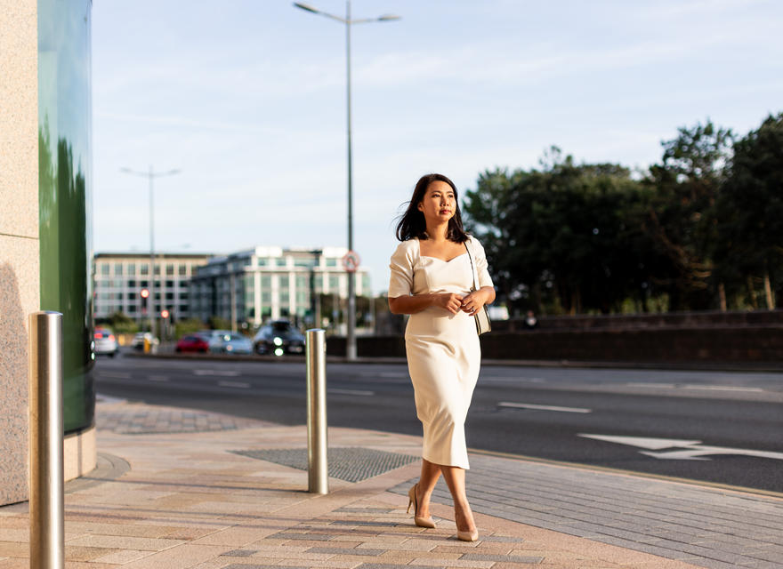 Businesswoman walking purposefully along a city pavement in soft evening light.