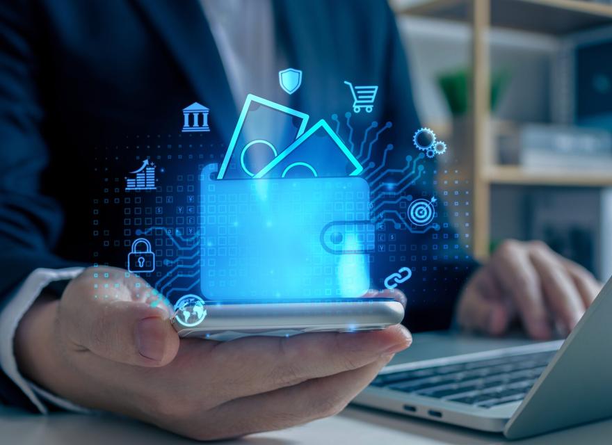 Man working on his laptop, holding a mobile phone, plus a digital wallet icon