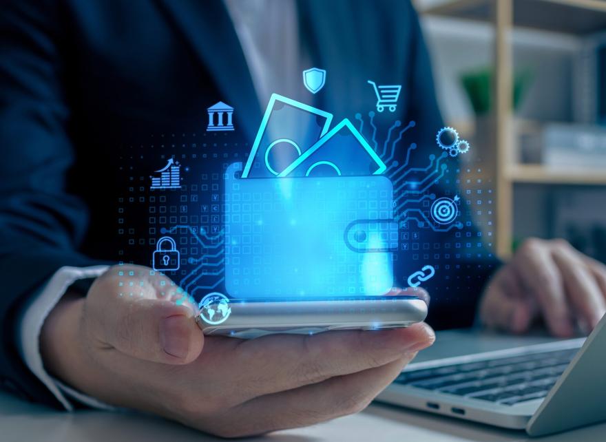 Man working on his laptop, holding a mobile phone, plus a digital wallet icon