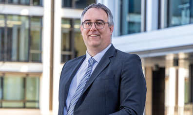 Gavin Carruthers, suited, smiling outside a building