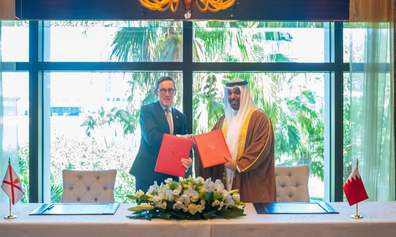 A politician in western business suit shakes hand with a politician in Arab attire whilst holding red folders