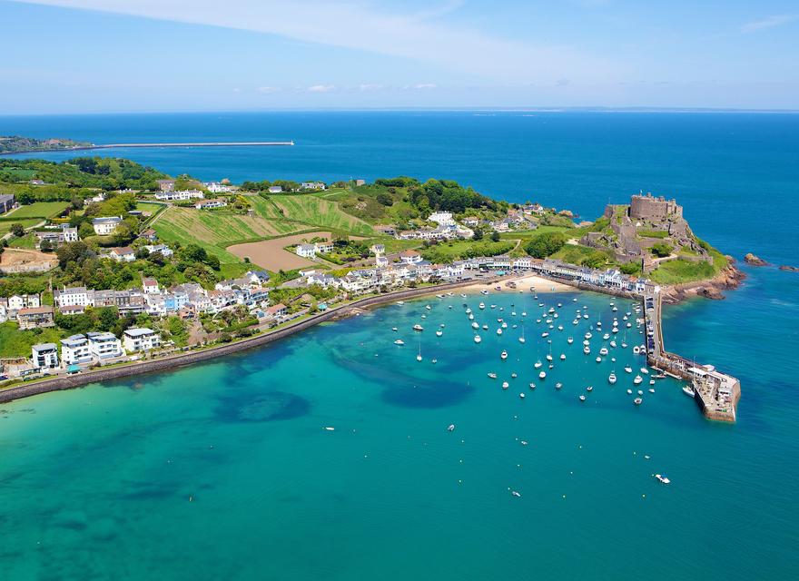 Aerial view of Mont Orgueil Castle, the pier and the boats moored up in the harbour on a sunny day in Jersey, C.I.