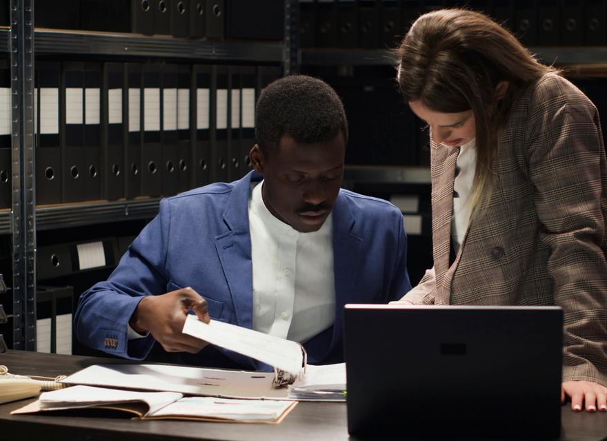 Two people conducting criminal investigation by collecting clues and information using, laptop and case files.