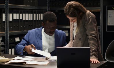 Two people conducting criminal investigation by collecting clues and information using, laptop and case files.