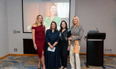 Four ladies in business attire in front of screen image of An Kelles